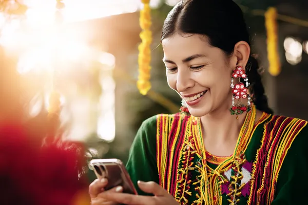 A cheerful woman in traditional clothing using her smartphone during a festive moment, showing how easily the DEAWUN app fits into everyday life.